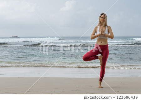 Full length portrait of healthy young woman doing yoga balance exercise at the beach. Copy space Full length portrait of healthy young woman doing yoga balance exercise at the beach. Copy space 122696439
