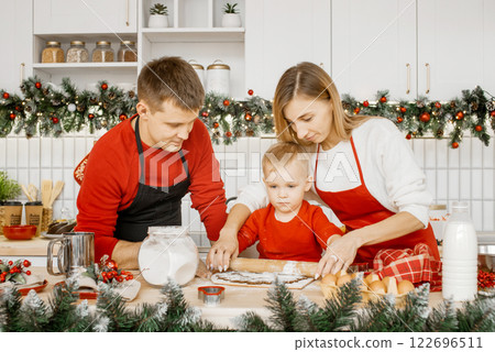 Happy family rolling out dough to bake Christmas cookies in the kitchen. Family Concept. Christmas concept Happy family rolling out dough to bake Christmas cookies in the kitchen. Family Concept. Christmas concept 122696511