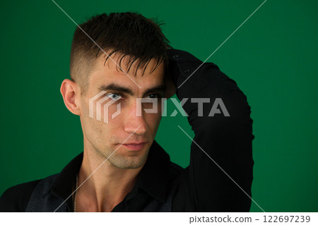Young man in a green shirt with a concerned expression, holding his head in his hands, isolated over green background. 122697239