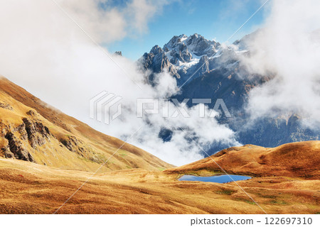Autumn landscape and snow mountains in beautiful cumulus clouds. Main Caucasian Ridge. Type Mount Ushba Mheyer, Georgia Autumn landscape and snow mountains in beautiful cumulus clouds. Main Caucasian Ridge. Type Mount Ushba Mheyer, Georgia 122697310
