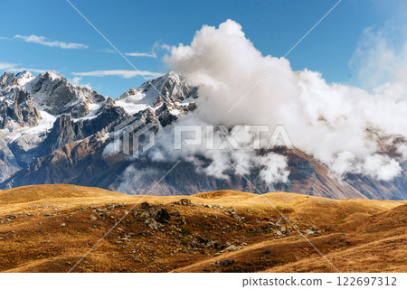 Autumn landscape and snow mountains in beautiful cumulus clouds. Main Caucasian Ridge. Type Mount Ushba Mheyer, Georgia 122697312