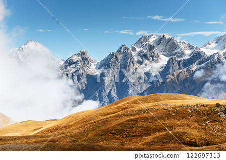 Autumn landscape and snow mountains in beautiful cumulus clouds. Main Caucasian Ridge. Type Mount Ushba Mheyer, Georgia 122697313