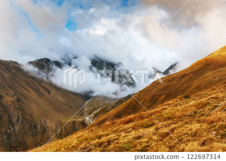 Autumn landscape and snow mountains in beautiful cumulus clouds. Main Caucasian Ridge. Type Mount Ushba Mheyer, Georgia 122697314