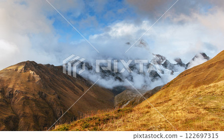 Autumn landscape and snow mountains in beautiful cumulus clouds. Main Caucasian Ridge. Type Mount Ushba Mheyer, Georgia Autumn landscape and snow mountains in beautiful cumulus clouds. Main Caucasian Ridge. Type Mount Ushba Mheyer, Georgia 122697315