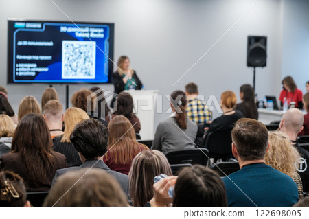 Speaker presenting at seminar with audience listening attentively in large conference room 122698005