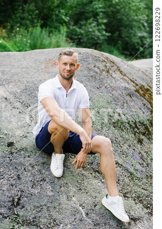 Relaxed Man Sitting Comfortably On Large Rock Outdoors Relaxed Man Sitting Comfortably On Large Rock Outdoors 122698229
