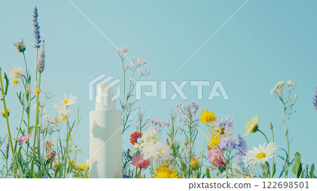 Vibrant wildflowers surrounding skincare bottle under clear blue sky 122698501