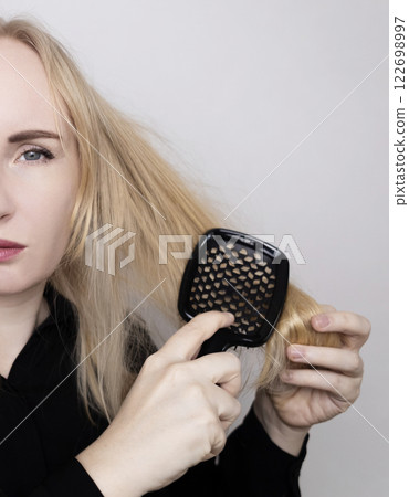 Blonde woman unhappy with her hair condition and trying to brush it. Bad hairstyle, tangled curly hair without using conditioner. Blonde woman unhappy with her hair condition and trying to brush it. Bad hairstyle, tangled curly hair without using conditioner. 122698997