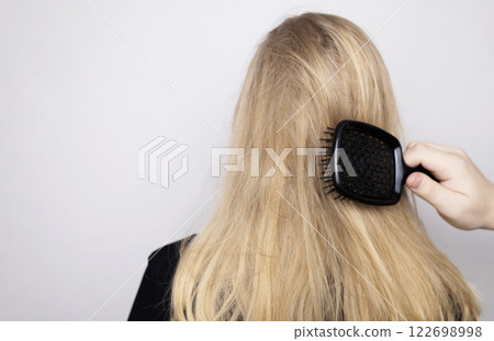 Blonde woman unhappy with her hair condition and trying to brush it. Bad hairstyle, tangled curly hair without using conditioner. 122698998