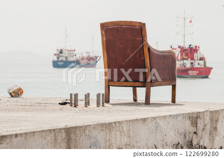 Lonely vintage armchair overlooks a calm sea with distant fishing boats. A serene, slightly melancholic coastal scene evoking themes of solitude and contemplation Lonely vintage armchair overlooks a calm sea with distant fishing boats. A serene, slightly melancholic coastal scene evoking themes of solitude and contemplation 122699280
