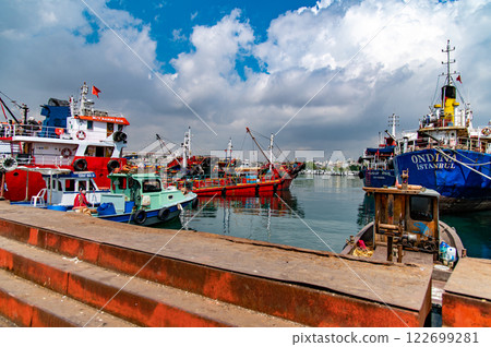 Colorful fishing boats bob gently in a tranquil harbor, under a vibrant sky. A rustic dock provides a foreground element, enhancing the idyllic scene Colorful fishing boats bob gently in a tranquil harbor, under a vibrant sky. A rustic dock provides a foreground element, enhancing the idyllic scene 122699281