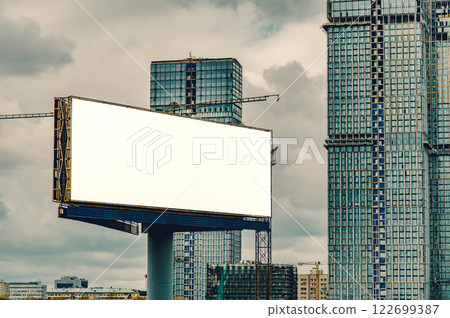 A modern urban landscape with a blank white billboard set against the backdrop of under-construction skyscrapers A modern urban landscape with a blank white billboard set against the backdrop of under-construction skyscrapers 122699387