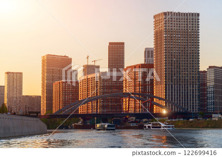 Golden hour cityscape at sunset, modern architecture reflected in calm water, bridge silhouette. Urban tranquility 122699416