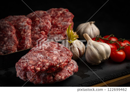 Juicy frozen hamburger patties ready for grilling. Close-up shot with fresh garlic and cherry tomatoes. Perfect for restaurant menus, recipe blogs, and food advertising 122699462
