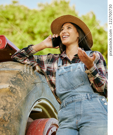 Agriculture, sustainability and farmer talking on phone while working on a farm with a tractor. Wellness, health and agro woman networking with a mobile while standing on a field in the countryside. Agriculture, sustainability and farmer talking on phone while working on a farm with a tractor. Wellness, health and agro woman networking with a mobile while standing on a field in the countryside. 122700730