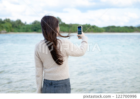 A woman taking a photo while looking at the sea 122700996