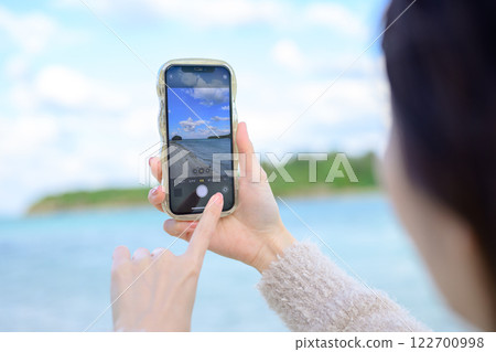 A woman taking a photo while looking at the sea 122700998