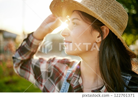 Farm, agriculture and woman farmer working in the field during spring at sunset to monitor growth. Wellness, sustainability and eco friendly female standing in a green, agro and sustainable garden. Farm, agriculture and woman farmer working in the field during spring at sunset to monitor growth. Wellness, sustainability and eco friendly female standing in a green, agro and sustainable garden. 122701371