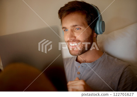 Man streaming movies online on digital tablet, watching series on technology in bedroom and listening to audio on headphones at night in bed at house. Person with smile reading social media post Man streaming movies online on digital tablet, watching series on technology in bedroom and listening to audio on headphones at night in bed at house. Person with smile reading social media post 122701627