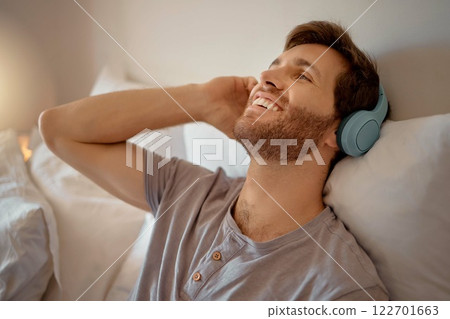 Man listening to music, podcast or radio with headphones at home while relaxing, smile and happy in his bedroom. Peaceful, freedom and young male streaming an online audio playlist enjoying weekend Man listening to music, podcast or radio with headphones at home while relaxing, smile and happy in his bedroom. Peaceful, freedom and young male streaming an online audio playlist enjoying weekend 122701663