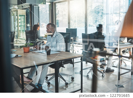 Business, office and work with a man sitting at his desk in a glass building and working with colleagues in the background. A busy corporate company with an employee and worker at a table for his job 122701685
