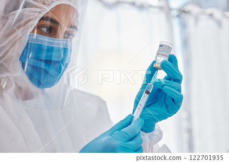 Medical scientist, doctor or healthcare worker in a safety suit ready to give the covid vaccine. Hospital employee holding, looking and working with care on a corona medicine vial at a hospital 122701935