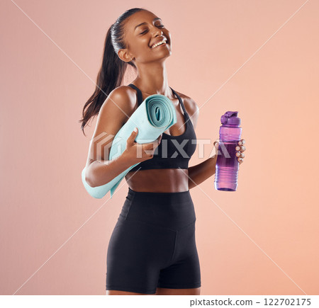 Happy, fitness and healthy while holding exercise mat and water bottle against peach studio background. Fit woman with slim body after exercise, training and sports workout and vitality healthcare 122702175