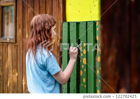 Cute teenage girl paints a building outdoors in the country, with her own hands, creativity, beauty, diy Cute teenage girl paints a building outdoors in the country, with her own hands, creativity, beauty, diy 122702425