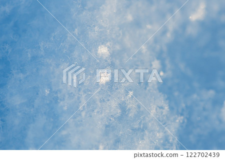 Close-up view of delicate snow crystals sparkling in the sunlight on a clear blue winter day, showcasing the intricate beauty of nature's frozen artistry 122702439