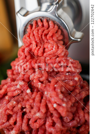 The concept of healthy and proper nutrition, cooking. A close-up view from above of red ground beef with streaks of fat, which comes out of the metal grinder in waves and takes up most of the photo 122702642