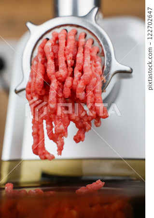 The concept of healthy and proper nutrition, cooking. Close-up side view of red ground beef with streaks of fat coming out of a metal grinder and falling into a transparent black plate below. High 122702647