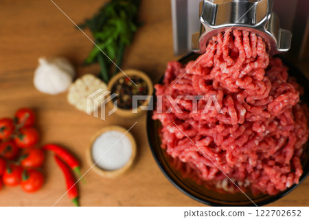 The concept of healthy eating, cooking. Close-up view from above of a dark plate with red minced beef with fat streaks that comes out of a metal meat grinder on a wooden background, spices, herbs and 122702652