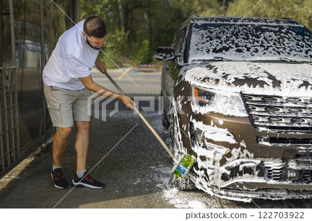 man washing a car in a self-service car wash station with wahing foam. Wash car self-service station man washing a car in a self-service car wash station with wahing foam. Wash car self-service station 122703922