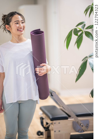 Smiling young woman holding a yoga mat 122704323