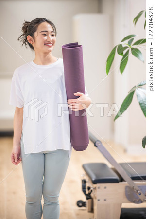 Smiling young woman holding a yoga mat Smiling young woman holding a yoga mat 122704328