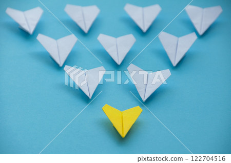 Straight view of yellow paper airplane origami leading other white airplanes on blue background with customizable space for text. Business and Leadership skills concept 122704516