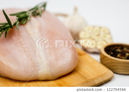 Chicken breast fillet with a sprig of rosemary lies on a wooden board, next to it is a wooden bowl with pepper seasoning and garlic on a white background. The concept of dietary dishes, a recipe for 122704566