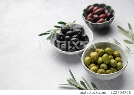 Bowls of green, black and kalamata olives with olive branches resting on a textured surface Bowls of green, black and kalamata olives with olive branches resting on a textured surface 122704768