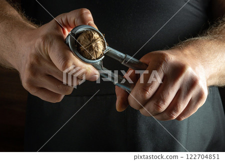Hands skillfully use a metal nutcracker to break open a walnut, revealing the rich, textured shell and inner nut. The warm ambiance adds a touch of tradition and craftsmanship to the moment. Hands skillfully use a metal nutcracker to break open a walnut, revealing the rich, textured shell and inner nut. The warm ambiance adds a touch of tradition and craftsmanship to the moment. 122704851