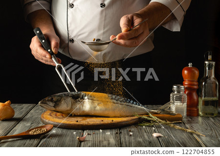 The chef prepares mackerel on a cozy hotel kitchen table. The concept of preparing fish food with aromatic paprika and spices. European cuisine 122704855