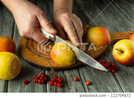 Hands expertly cut ripe apples on a rustic wooden board surrounded by vibrant citrus fruits. The atmosphere feels warm and inviting, perfect for a culinary adventure 122704872