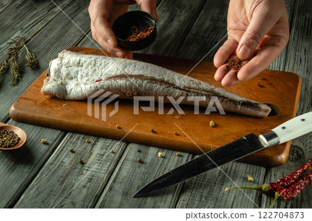 Hands expertly sprinkle spices over a fresh, whole fish on a wooden cutting board, creating a culinary masterpiece. The warm, rustic atmosphere enhances the cooking experience Hands expertly sprinkle spices over a fresh, whole fish on a wooden cutting board, creating a culinary masterpiece. The warm, rustic atmosphere enhances the cooking experience 122704873