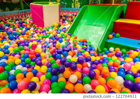 Bright green slide leading into a colorful and fun ball pit for kids. 122704911