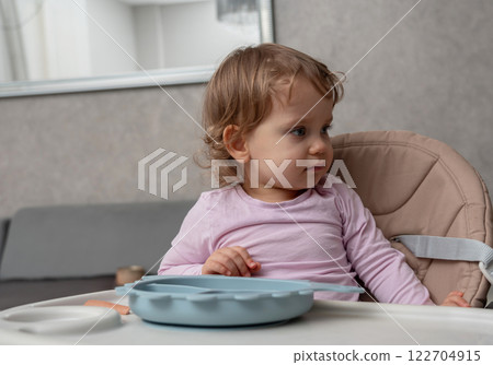 A curious toddler distracted during mealtime, observing something with focused attention. 122704915