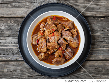 beef stew in a white bowl on rustic wooden table 122705484