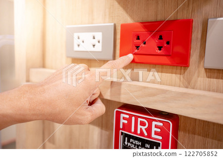 Hand pointing at red electric socket or power plug outlet on wooden wall with a fire alarm switch 122705852