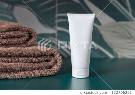 White cream tube near brown towels in dark green tropical bathroom close up, cosmetic mockup White cream tube near brown towels in dark green tropical bathroom close up, cosmetic mockup 122706291