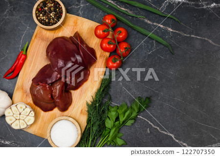 Top view with text space on raw chicken liver on wooden board surrounded by red hot peppers, garlic, tomatoes, seasonings and salt in wooden bowls and herbs on a dark background. The concept of Top view with text space on raw chicken liver on wooden board surrounded by red hot peppers, garlic, tomatoes, seasonings and salt in wooden bowls and herbs on a dark background. The concept of 122707350