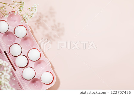 White eggs in pink container adorned with delicate floral accents on soft pastel pink background. Minimalist and elegant concept perfect for holiday Easter celebrations and spring themes. Copy space 122707456