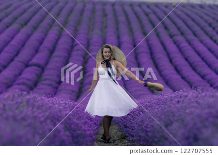 A woman in a white dress is standing in a field of purple flowers A woman in a white dress is standing in a field of purple flowers 122707555